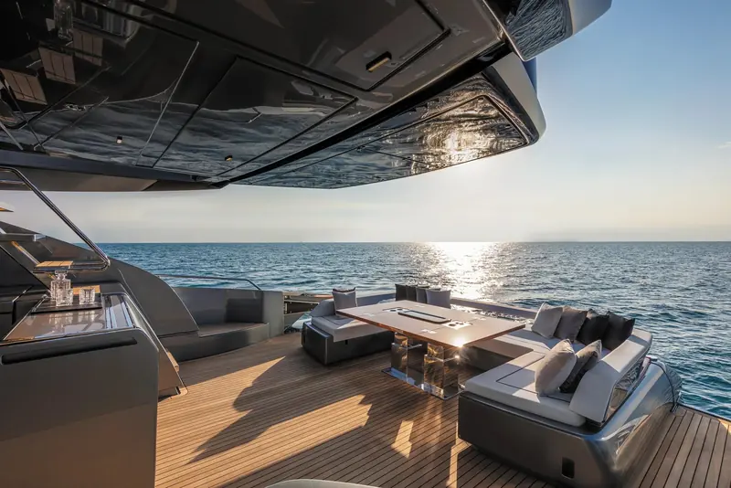 A shaded aft dining table sits under the flybridge overhang, set for guests at anchor.