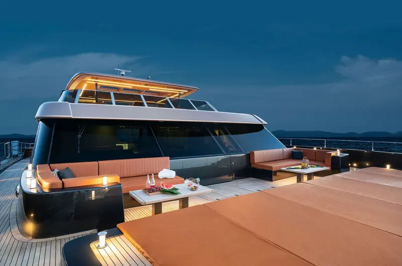 The aft deck lounge at dusk, one of several open-air entertaining areas spread across the catamaran's wide beam.