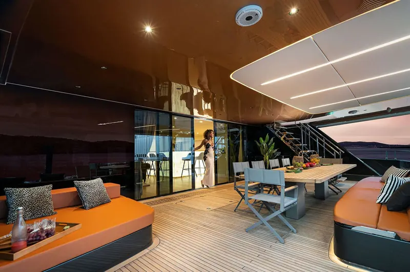 The saloon at dusk, its glazing running the full width of the catamaran's beam - the volume a monohull of comparable length cannot match.