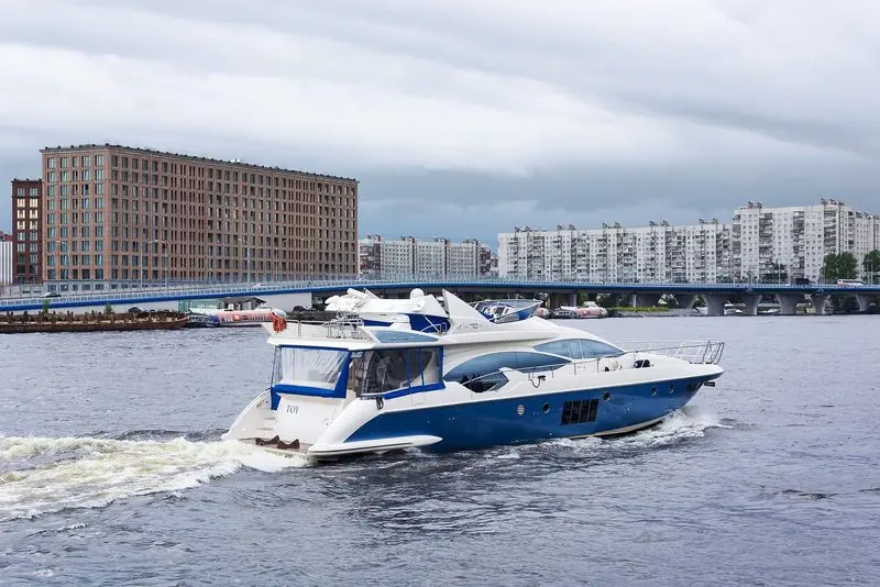 Blue hulled and running hard, a production flybridge yacht crosses a city river.