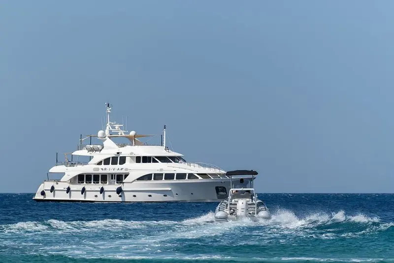 A tender runs past a classic Benetti motor yacht at anchor off Tinos, Greece