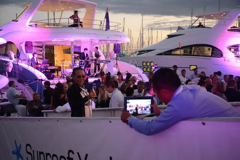 Dusk reception between two Sunreef motor yachts at the Cannes Yachting Festival, the docks crowded with guests