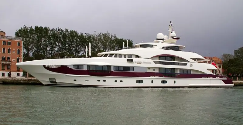 A cream hull with a burgundy stripe sits alongside in Venice under a storm sky.