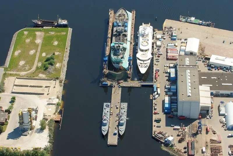 Yachts and grey hulls share one basin at a north German yard that builds both.