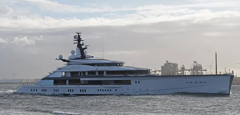 Backlit on the Nieuwe Waterweg, a superyacht heads for open water with wind turbines behind her.