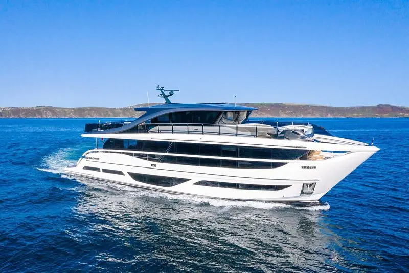 A Princess X95 motor yacht underway off a green coastline in flat blue water