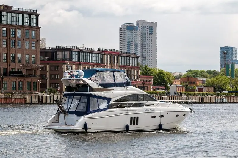 A Princess flybridge motor yacht named Mirage cruising past a brick waterfront on the Khimki Reservoir