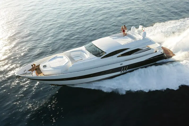 Seen from above, a Pershing 90 runs across backlit water with guests on the foredeck.