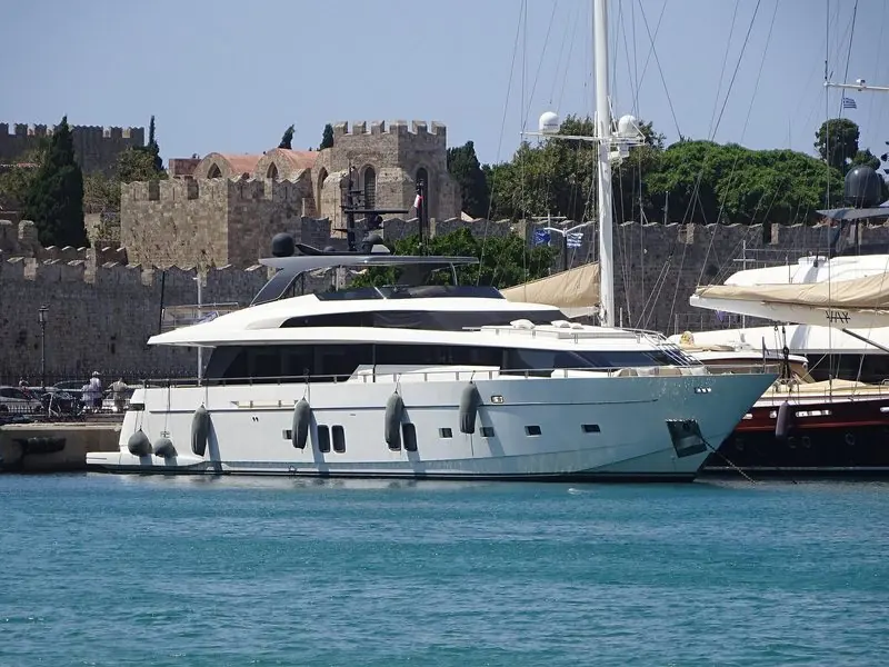 The medieval walls of Rhodes rise behind a Sanlorenzo on the town quay.