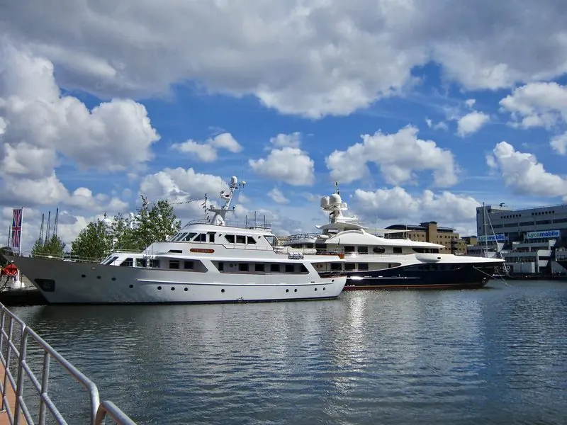 A classic white motor yacht and a modern dark-hulled superyacht berthed side by side in Canary Wharf, London