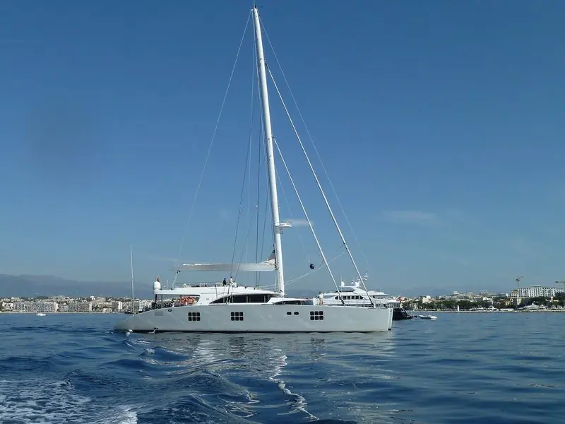 Sails stowed, a large Sunreef catamaran lies off the Cote d'Azur with the coast behind.