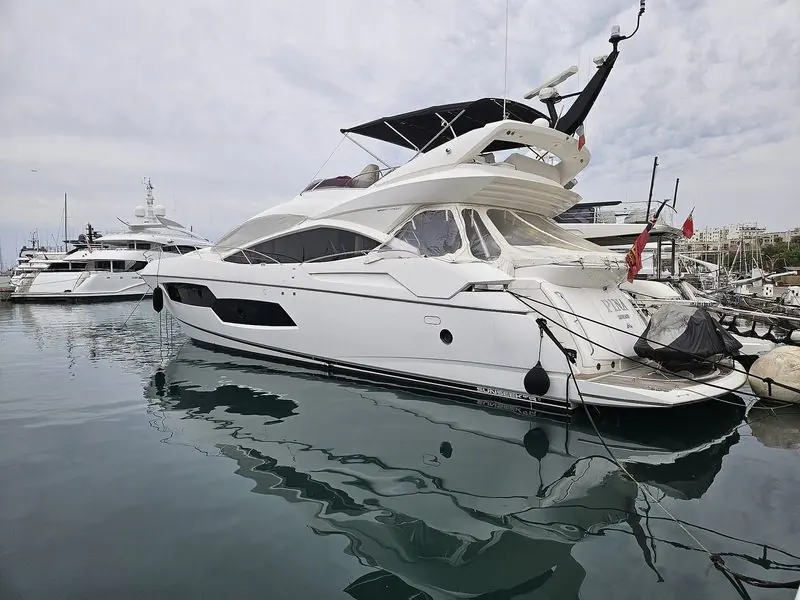 Flat grey water in a Mediterranean marina, with a white Sunseeker still under her covers.